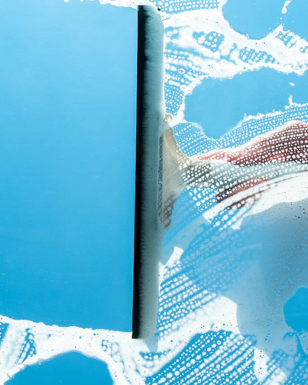 Squeegee wiping soapy water from a window, leaving a clear and streak-free surface