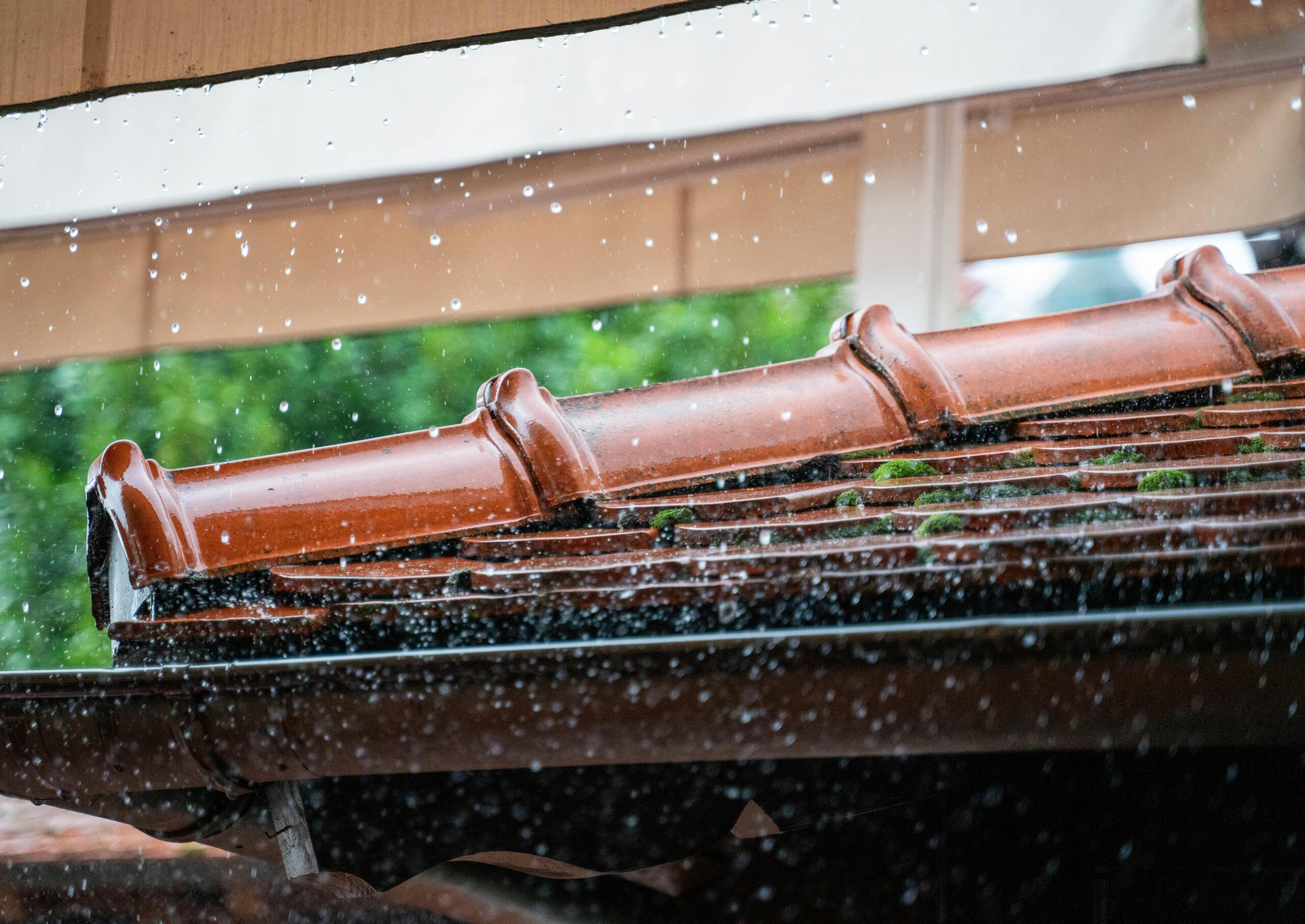 Rainwater overflowing from a clogged roof gutter during a heavy downpour